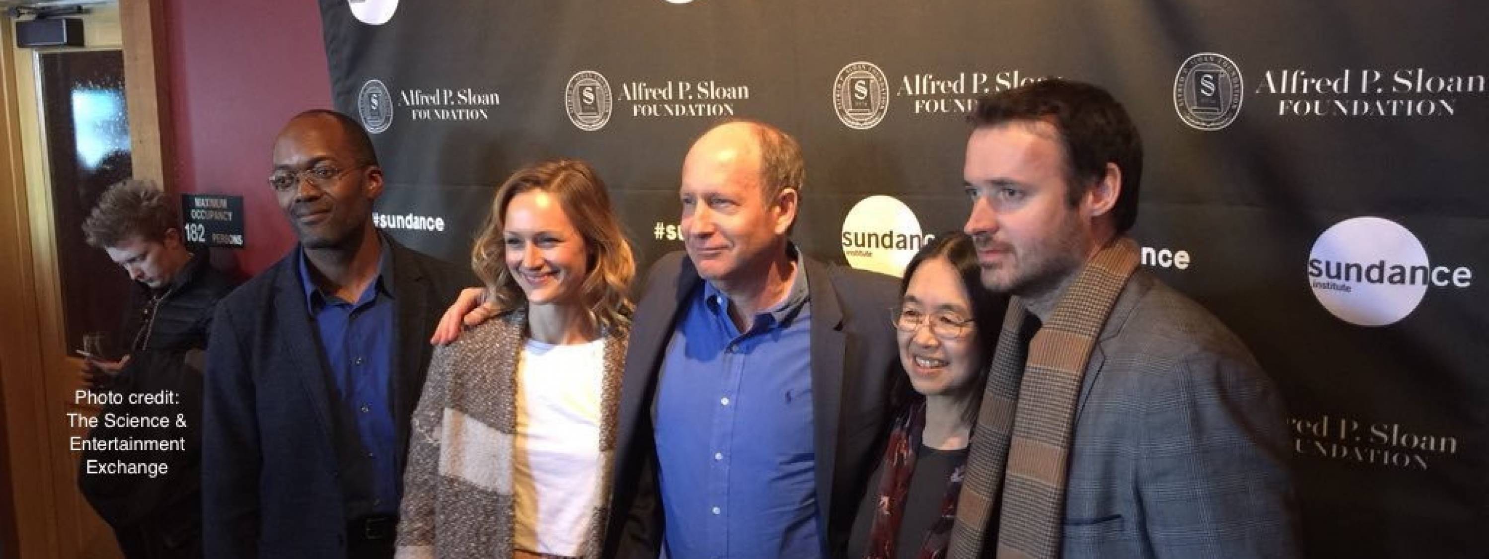 A photo of people smiling in front of a sundance film festival banner.