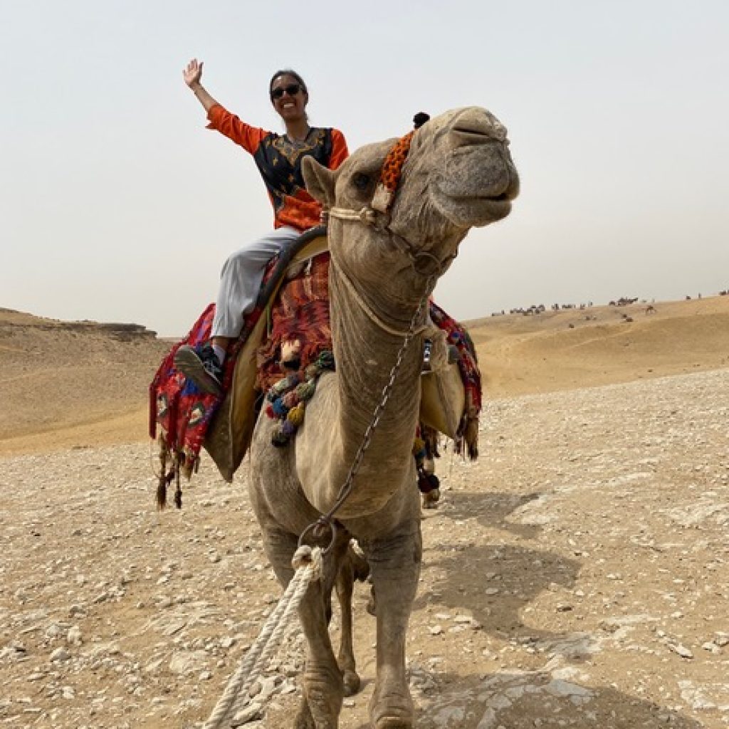 Shoumita riding on a camel in a desert landscape.