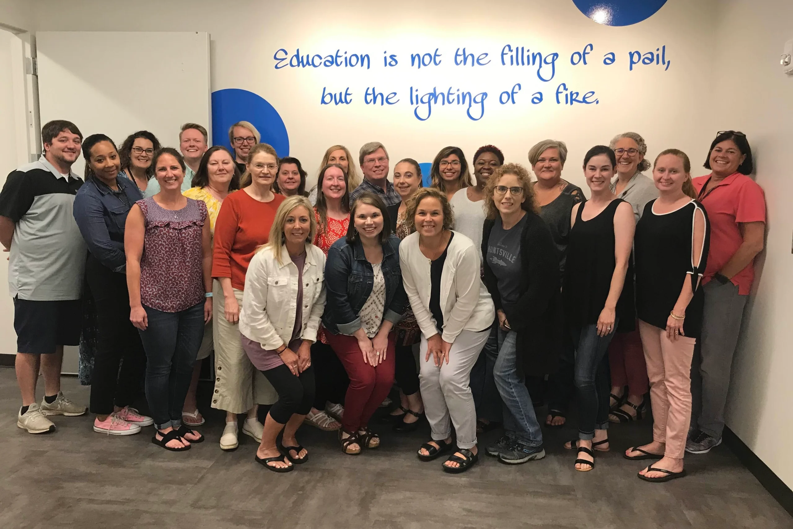 Workshop participants pose in front of a wall that reads “Education is not the filling of a pail, but the lighting of a fire”.