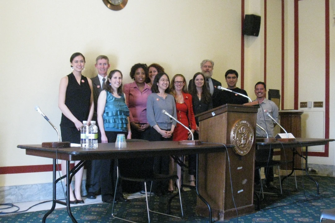 Group photo of the PGED team and colleagues standing behind a lecture stand with a seal of the United States House of Representatives.