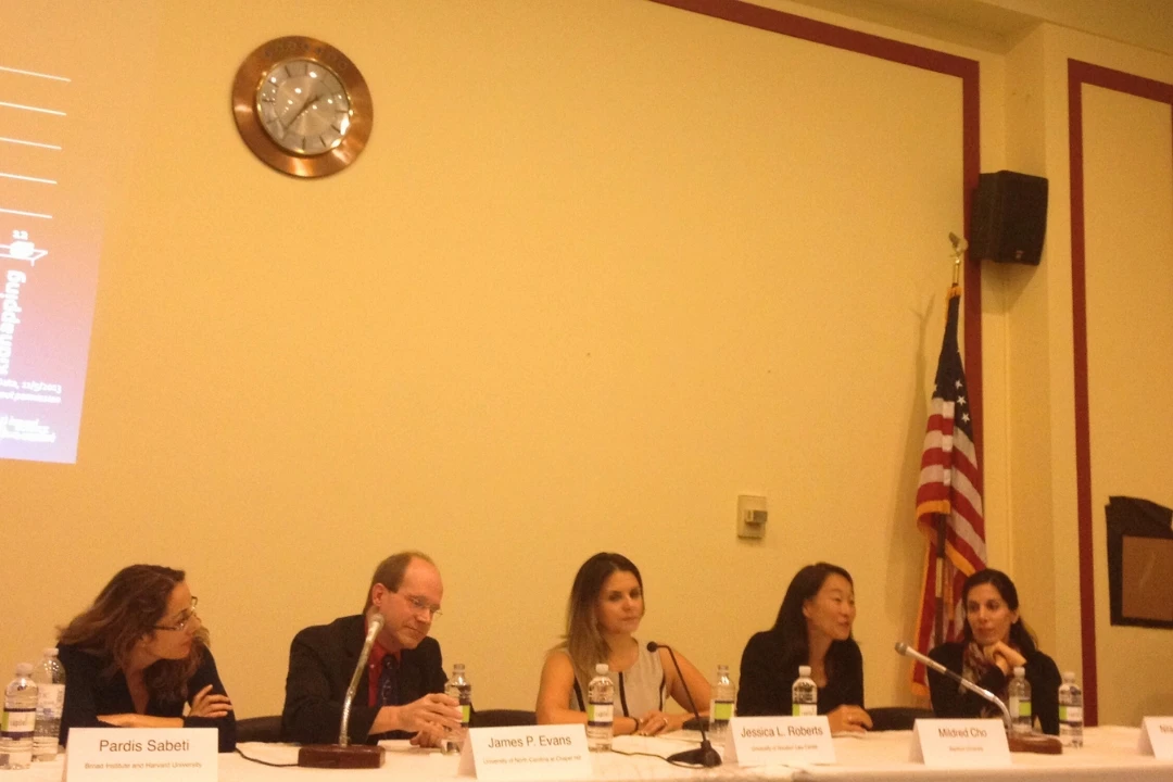 Panel of speakers sitting at a table in front of a projector screen.