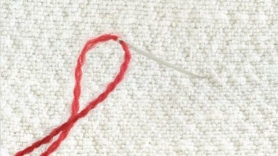 Red thread through a sewing needle embedded in white fabric.