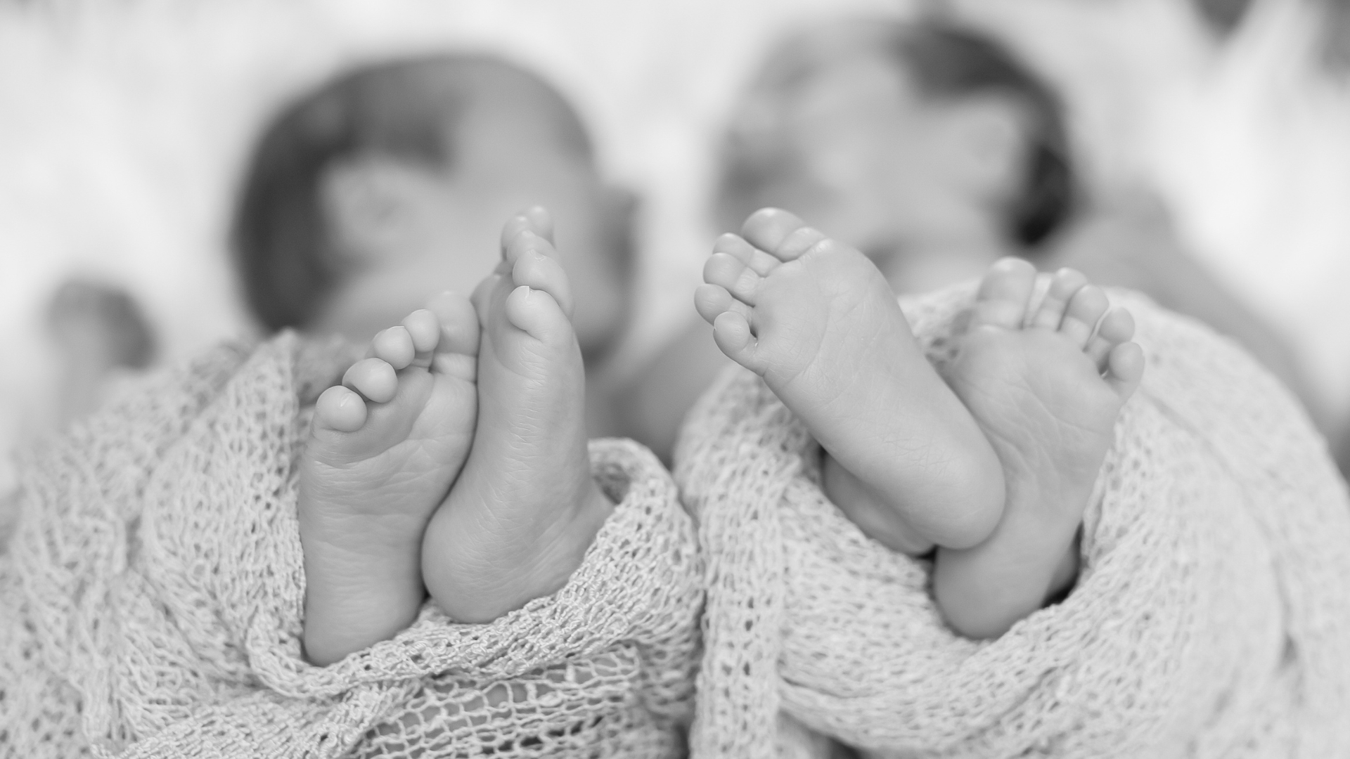 The feet of infant twins stick out from swaddling blankets.