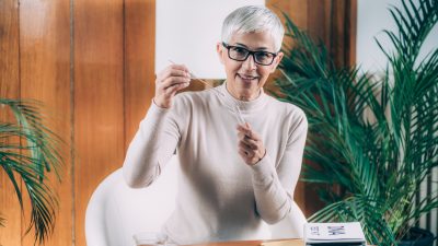 A woman with short grey hair and glasses holds a cotton swab used to collect DNA before inserting it into a tube.