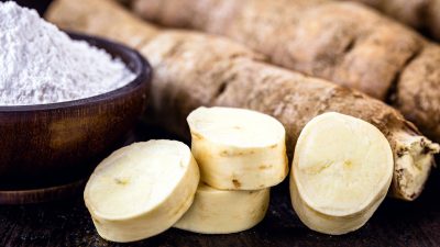 A bowl of white cassava powder next to the raw root and some cut up pieces.