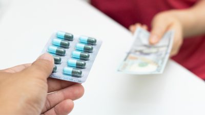 A person is holding pills in exchange for money.